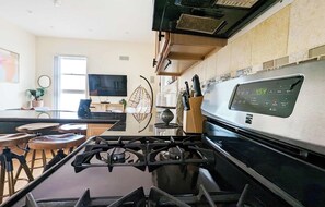 A modern kitchen with a gas stove, stainless steel appliances, and a dining area with stools.