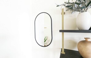 A minimalist room with a black-framed mirror, a white vase, and a potted plant on a black shelf.