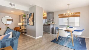A modern living room with a blue sofa, a dining area with white chairs, and a kitchen in the background. - 3BR Townhouse in Prime Manhattan Beach Location (Manhattan Beach)