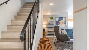 A staircase with wooden steps and a black railing, leading to a living area with a blue sofa, a wooden bench, and a wall-mounted shelf with decorative items. - 3BR Townhouse in Prime Manhattan Beach Location (Manhattan Beach)