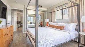 A modern bedroom with a four-poster bed, a wooden dresser, and a view of the adjacent room. - 3BR Townhouse in Prime Manhattan Beach Location (Manhattan Beach)
