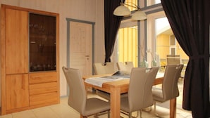 Un área de comedor con una mesa y sillas de madera, un armario con puertas de cristal y una ventana con cortinas.