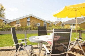 Una terraza con mobiliario exterior, incluyendo sillas y una mesa, bajo un paraguas amarillo grande.