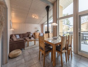Un espacio habitable amplio con techo de madera, una mesa de comedor con sillas, un sofá y un ventanal con vistas al exterior.