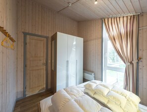 Un dormitorio con paredes de madera, una cama con ropa blanca, un armario y una ventana con cortinas.