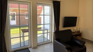 A room with a black leather chair, a flat-screen TV mounted on the wall, and a sliding glass door leading to an outdoor area with a patio. - Doppelhaushalfte in Burhave (Butjadingen)
