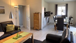 A modern living room with a sofa, coffee table, and a dining area with a table and chairs. - Doppelhaushalfte in Burhave (Butjadingen)