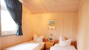 Une chambre avec deux lits en bois, une petite table de chevet avec une lampe et une fenêtre avec des rideaux.