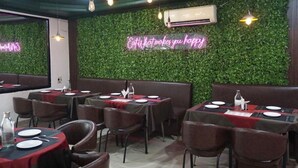 A restaurant interior with tables set for dining, a neon sign on the wall, and hanging pendant lights. - Hotel Clay Inn (Sohna)