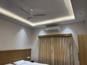 Una habitación de hotel con cama, ventilador de techo, aire acondicionado y cortinas.