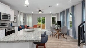 Una cocina moderna con una isla central, comedor con sillas y un ventilador de techo.