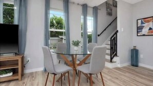 Una sala de estar moderna con una mesa de comedor de cristal rodeada de sillas, una escalera y un televisor sobre un mueble de madera.