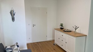 A room with a wooden floor, a white door, a white cabinet with drawers, a blue sofa with a patterned cushion, and a wall-mounted light fixture. - Pempelforter Domicile (Düsseldorf)