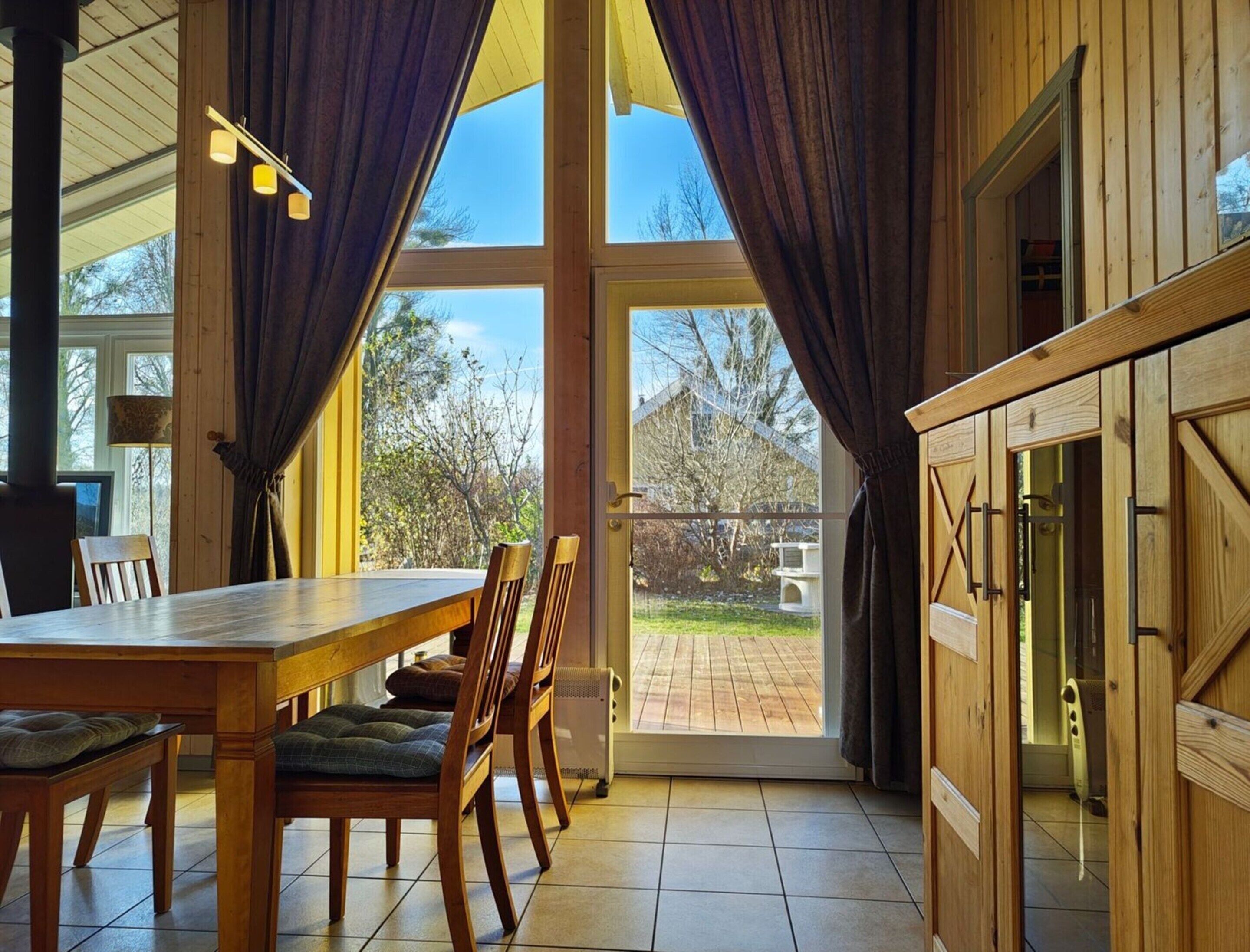 A dining area with a wooden table and chairs, a large window with curtains, and a view of the outdoors.