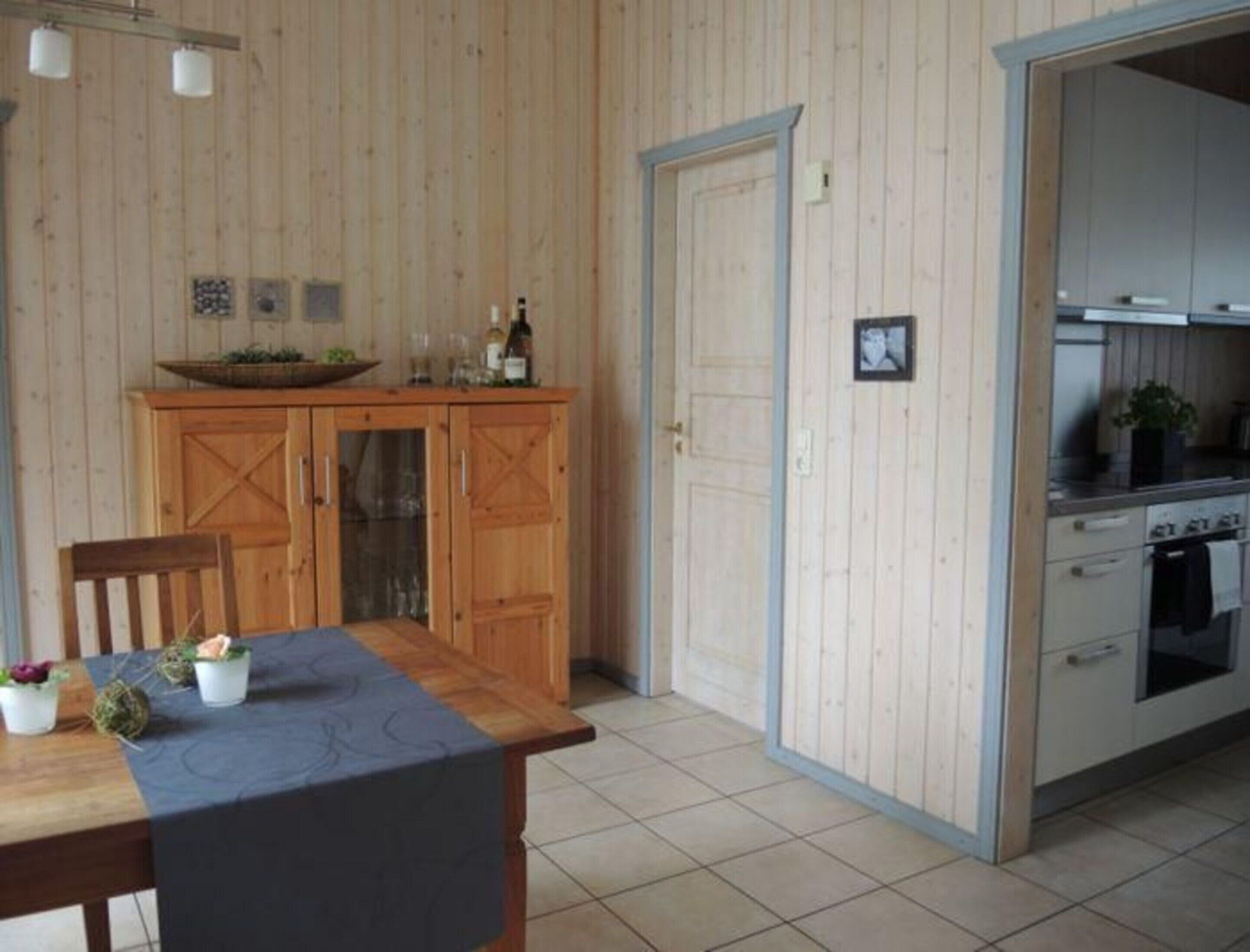 Ett kök med träskåp, ett matbord med stolar och ett klinkergolv.