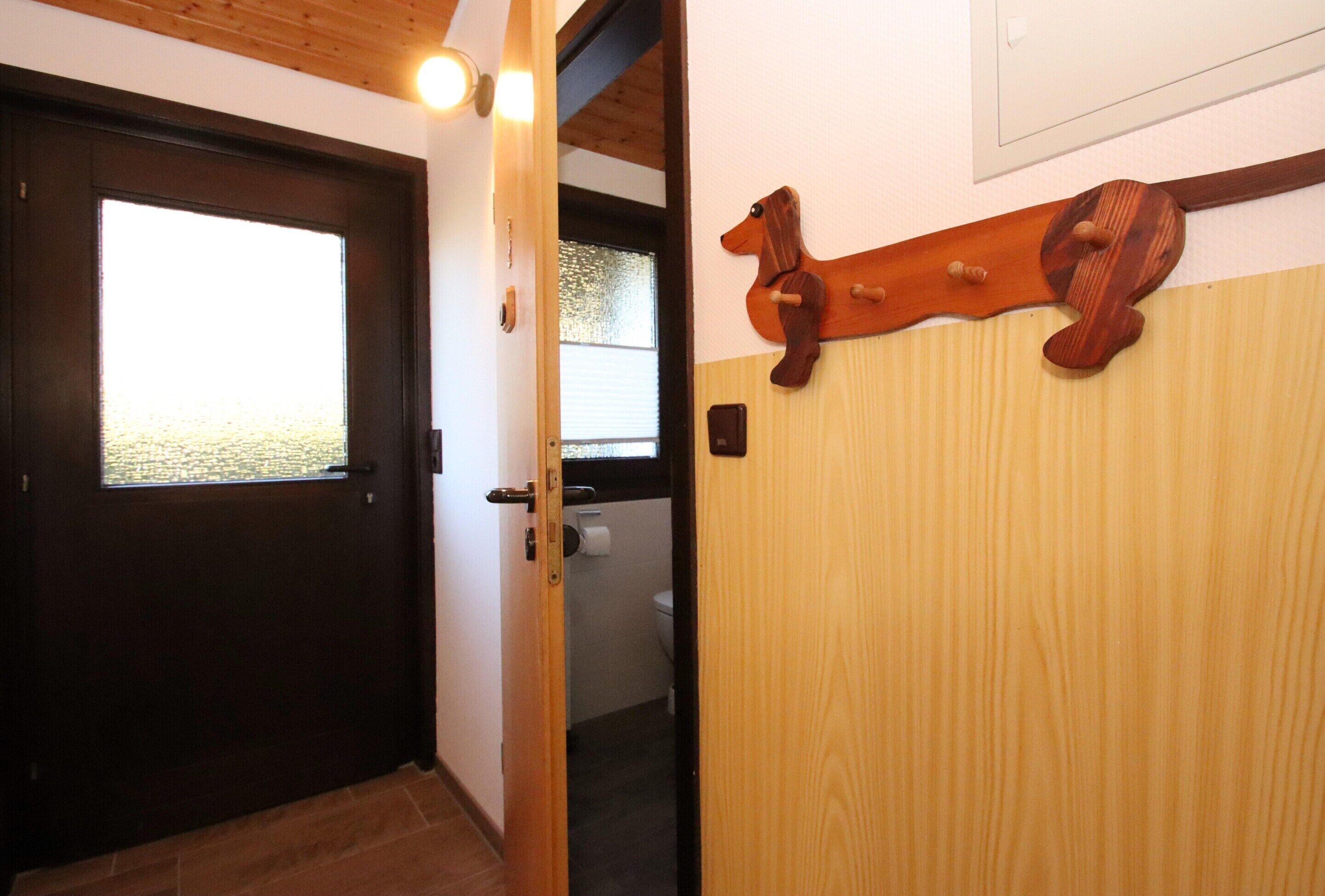 A wooden door with a window, a wooden coat rack, and a toilet visible through an open door.