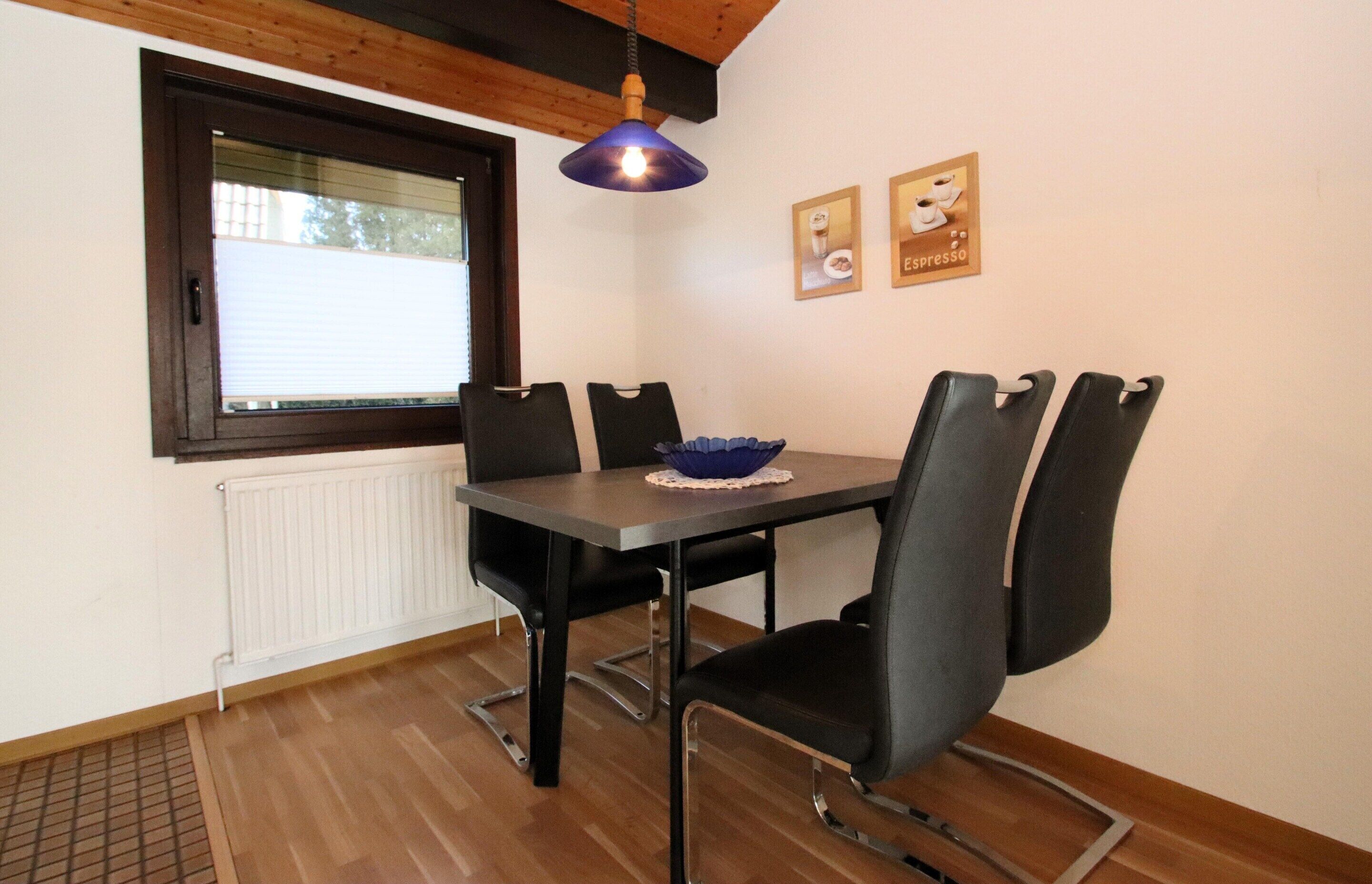 A dining area with a table, chairs, a blue pendant light, and two framed pictures on the wall.