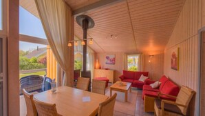A cozy room with a wooden ceiling, a dining table with chairs, a red sofa, and wicker chairs. - Exklusives Skandinavisches Ferienhaus (Rechlin)