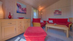 A cozy room with wooden walls, a red sofa, a wooden cabinet, and a red bench. - Exklusives Skandinavisches Ferienhaus (Rechlin)