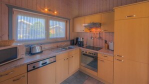 A compact kitchen with wooden cabinets, a microwave, a toaster, a sink, and a stove. - Exklusives Skandinavisches Ferienhaus (Rechlin)