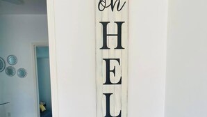 Un corridoio con un cartello verticale che riporta la scritta 'oh HELLO' e due piante in vaso gialle.