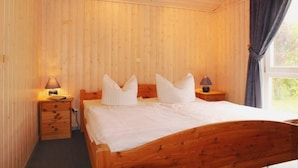Un dormitorio con paneles de madera, una cama, dos mesitas de noche y una ventana con cortinas.