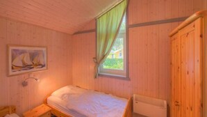 A wooden cabin room with a single bed, a nightstand, a radiator, and a painting on the wall. - Ferienhaus mit Sauna im Ferienpark Mirow (Mirow)