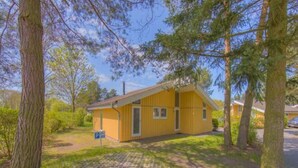 A yellow building with a single door and two windows, surrounded by trees and a paved area. - Ferienhaus mit Sauna im Ferienpark Mirow (Mirow)