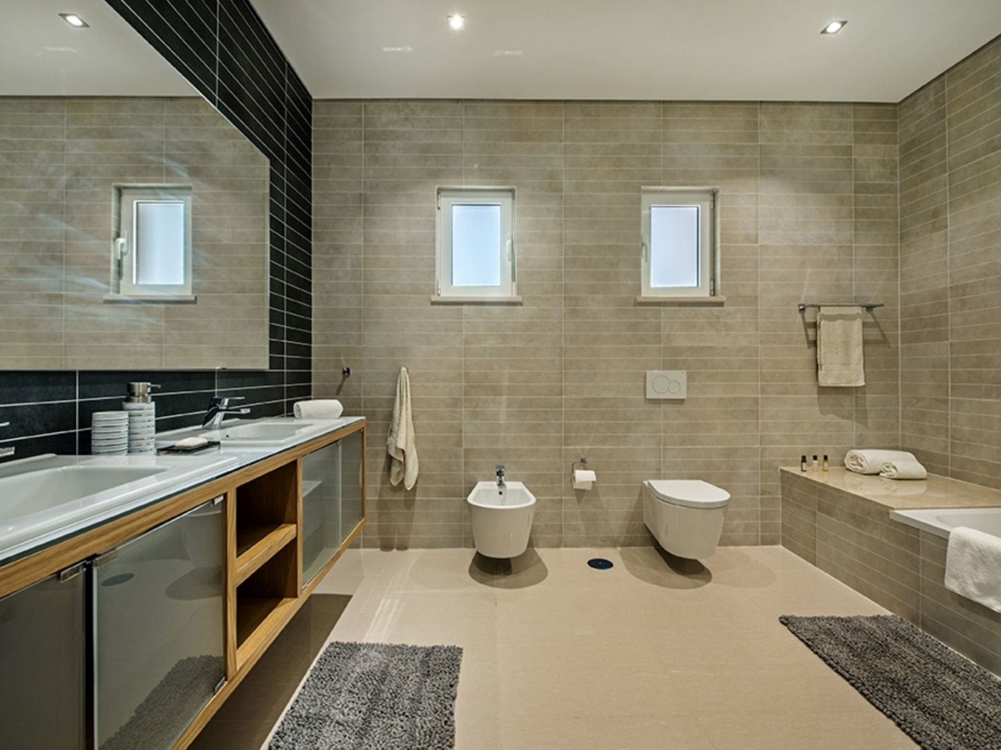 Une salle de bain moderne avec un grand miroir, deux lavabos, des toilettes et une baignoire.