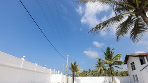 A swimming pool with a clear blue sky, palm trees, and a white building with a red roof. - Palazzo Beach Hikkaduwa (Hikkaduwa)