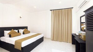 A modern hotel room with a black bed, beige curtains, a small desk with a microwave, and a mirror. - Palazzo Beach Hikkaduwa (Hikkaduwa)