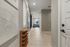 Un pasillo con un banco de madera, una pared blanca con diseño texturizado y una pared gris con textura.