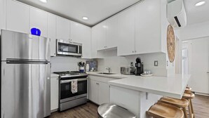 A modern kitchen with stainless steel appliances, a microwave, and wooden stools. - Mission Beach w/ OceanViews Surfboards Parking AC (San Diego)