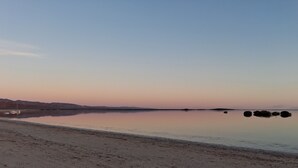 Ein ruhiger See mit einem Sandstrand und sanften Hügeln im Hintergrund.