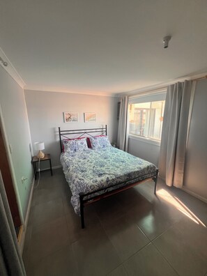 A bedroom with a bed, a nightstand, a lamp, and a window with curtains. - Beachfront Bliss with Stunning Eyre Peninsula Views (Miranda)