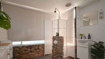 A bathroom with a stone sink, a shower with a glass door, and a white vanity with a mirror.