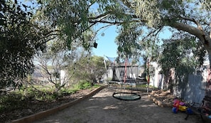 Ein Garten mit Schaukel, Trampolin und einem umzäunten Spielbereich.