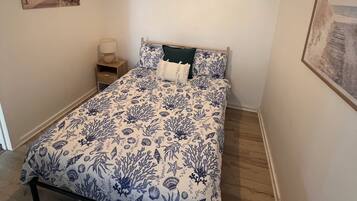 Een slaapkamer met een bed, nachtkastje, lamp en schilderij aan de muur.