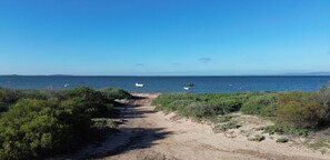 Ein Küstenpfad, der zum Meer führt, mit spärlicher Vegetation und blauem Himmel.