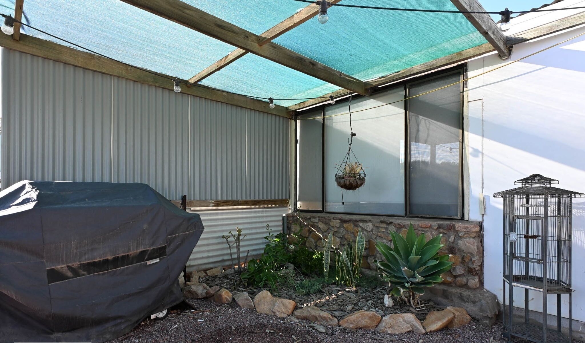 A covered outdoor area with a barbecue grill, hanging plants, and a birdcage.
