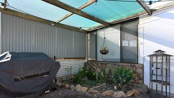 A covered outdoor area with a barbecue grill, hanging plants, and a birdcage.