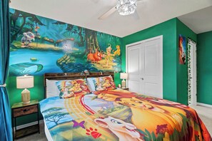 Un dormitorio con un mural, paredes verdes, una puerta blanca y una cama con un edredón colorido.