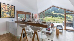 Een moderne keuken met een groot raam met uitzicht op een schilderachtig landschap, een eethoek met een houten tafel en een gezellige zithoek met een mooi vergezicht.