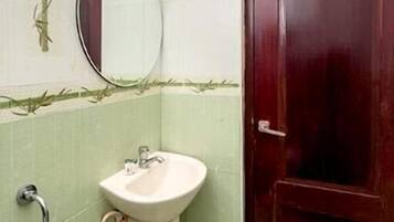A bathroom with a white sink, a mirror, a showerhead, and a wooden door.