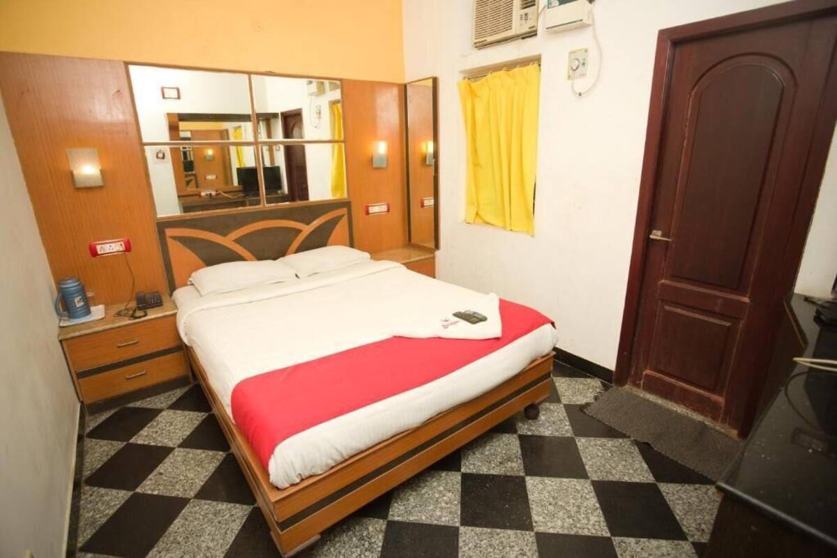 A hotel room with a bed, a mirror, a wardrobe, a door, and a check-in counter.