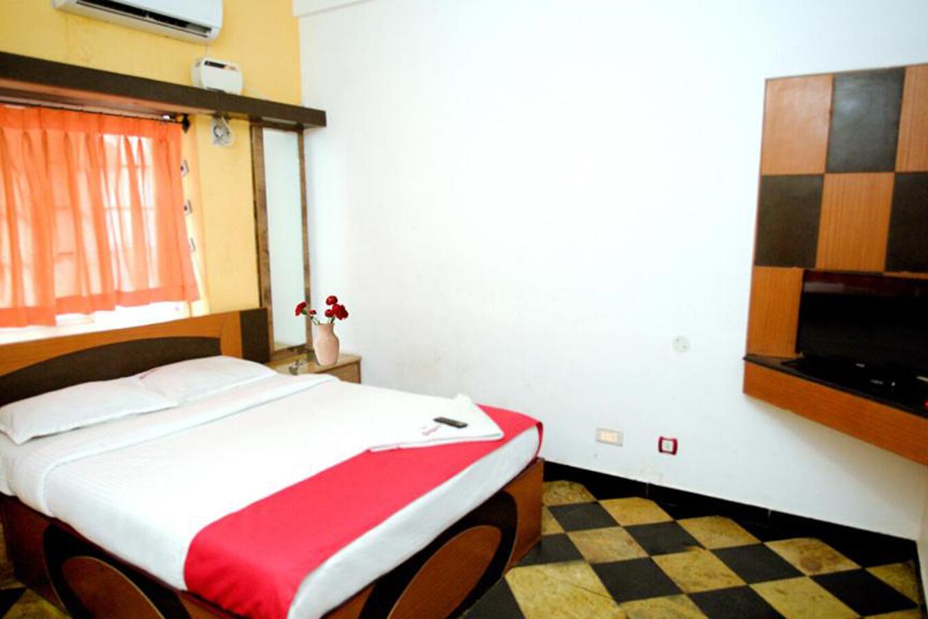 Une chambre d’hôtel avec un lit, un téléviseur fixé au mur et un sol à carreaux.