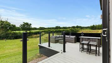 Relax on the deck with a sofa and bar stools, overlooking a serene lawn and tree line.