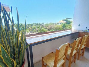 A balcony with a view of greenery and buildings, a potted plant, and a wooden chair. - Punta Colibrí (Brisas de Zicatela)