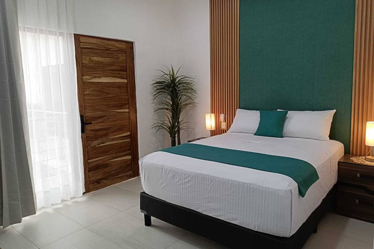 A bedroom with a bed, a nightstand, a potted plant, and a wooden door.