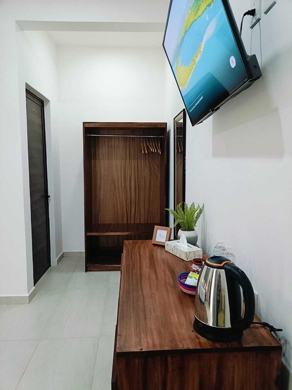 A room with a wooden desk, a television mounted on the wall, a wardrobe, and a small plant. - Punta Colibrí (Brisas de Zicatela)